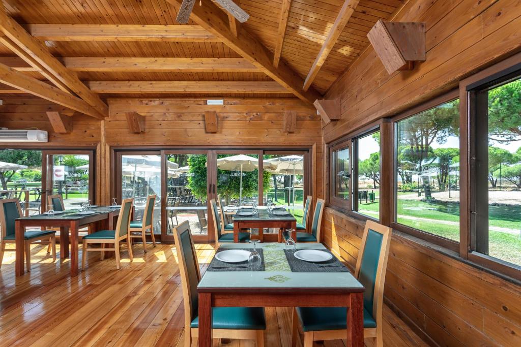 Koka restorāna interjers ar plašiem logiem un elegantām galdiem, kas piedāvā skatu uz dārzu un terasi. Gaisīga un silta atmosfēra, ideāli piemērota ēdienreizēm un socializēšanai.