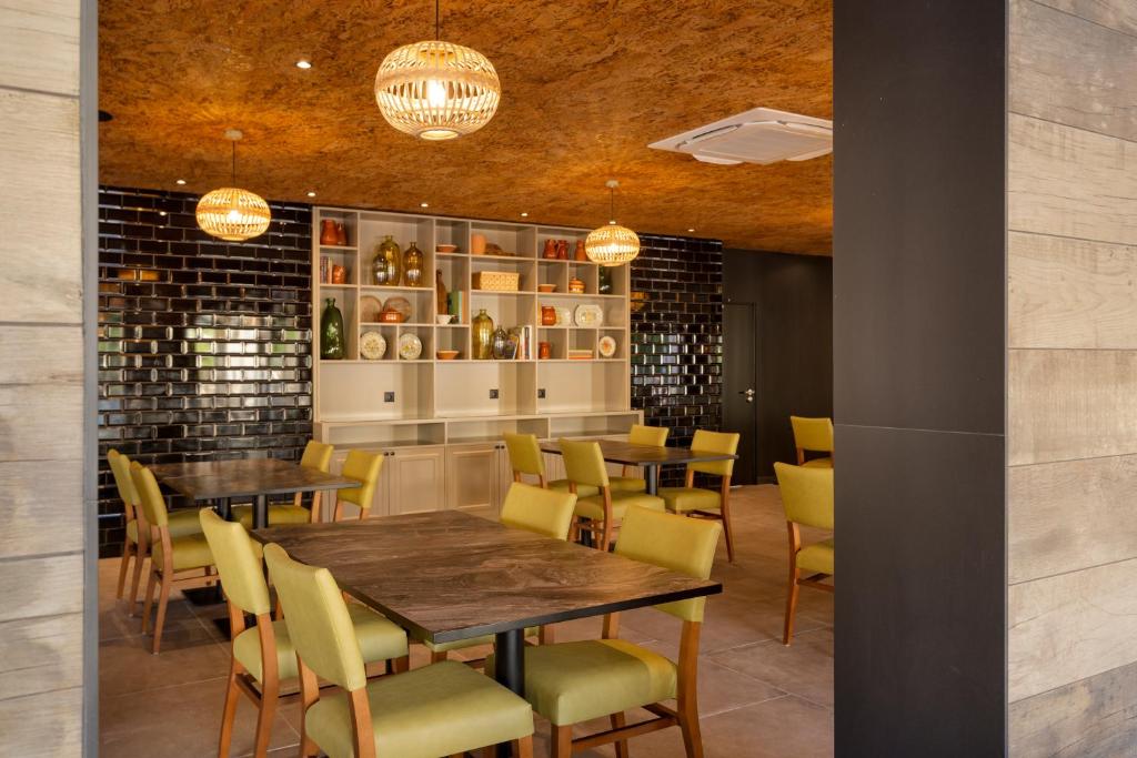 Mūsdienīgs restorāns ar elegantiem zaļiem krēsliem un akcentējošu melnu flīžu sienu, kas papildina gaišo mēbeļu dizainu un siltu apgaismojumu.