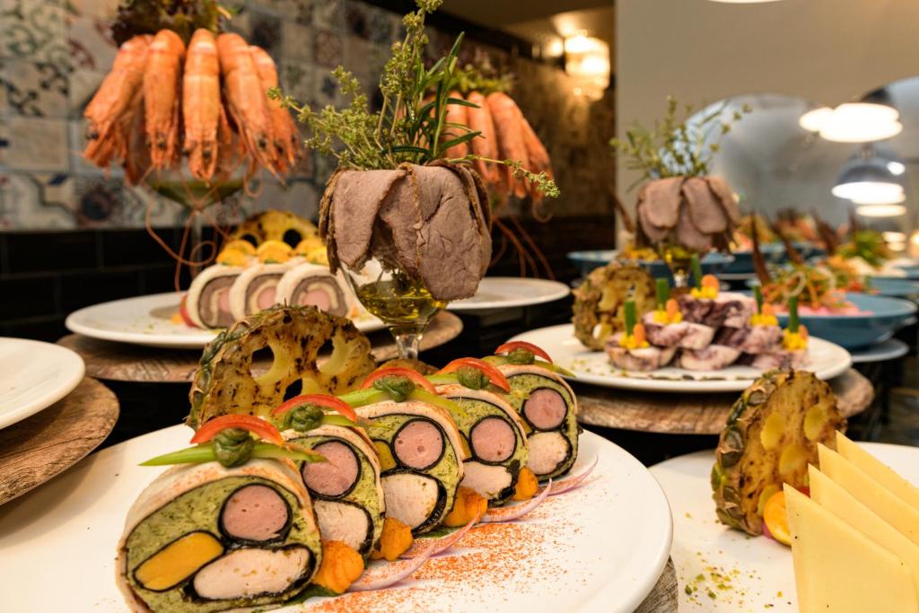 Skaisti noformēti ēdieni ar gaļu, garnelēm un dārzeņiem, kas izkārtoti uz šķīvjiem, radot krāšņu un apetītlīgu izskatu. Šī gourmet prezentācija ir lielisks piemērs elegantiem kulinārijas mākslas darbiem.