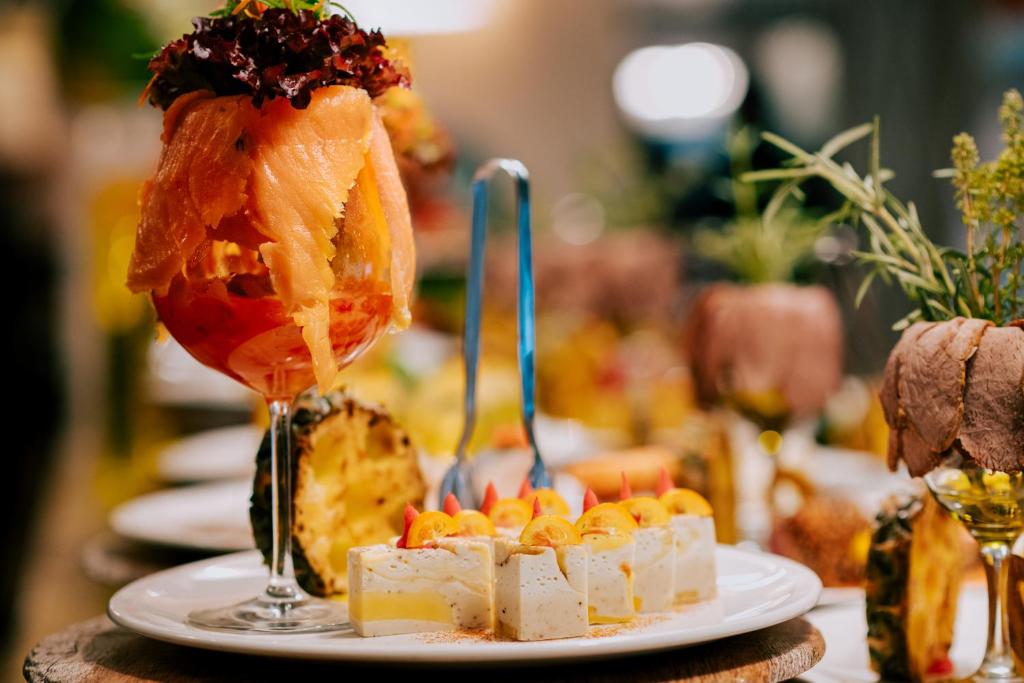 Elegantiem pasniegti ēdieni, tostarp zivs un deserta kārtojums, uz galda rotā ziedus un augļus. Ideāli piemērots svinīgām maltītēm.