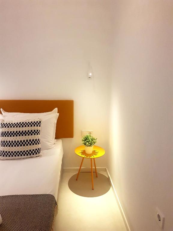 Mūsdienīga guļamistaba ar gultu un spilvenu, uz kura ir ģeometrisks raksts, un dzeltenu galdiņu ar augu. Gaisma rada siltu un mājīgu atmosfēru.