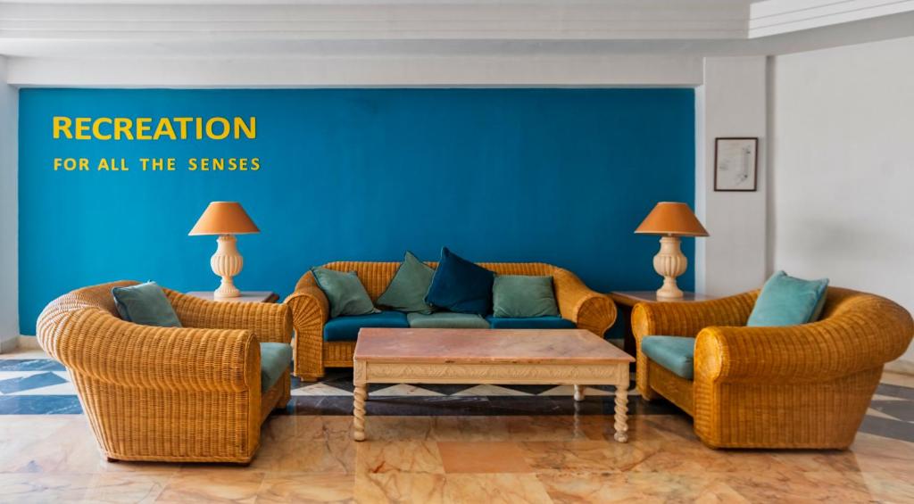 Skaista atpūtas zona ar vītinātiem mēbeļu komplektiem un spilveniem, kas kontrastē ar spilgti zilo sienu. Uz sienas ir rakstīts "RECREATION FOR ALL THE SENSES".