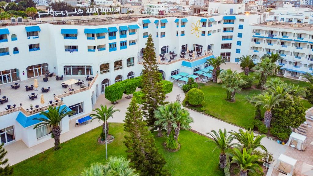 Viesnīcas komplekss ar zilo jumtu un plašiem dārziem, kas ieskauj terasi ar āra mēbelēm. Apkārt aug palmām un labi koptiem zaļumiem.