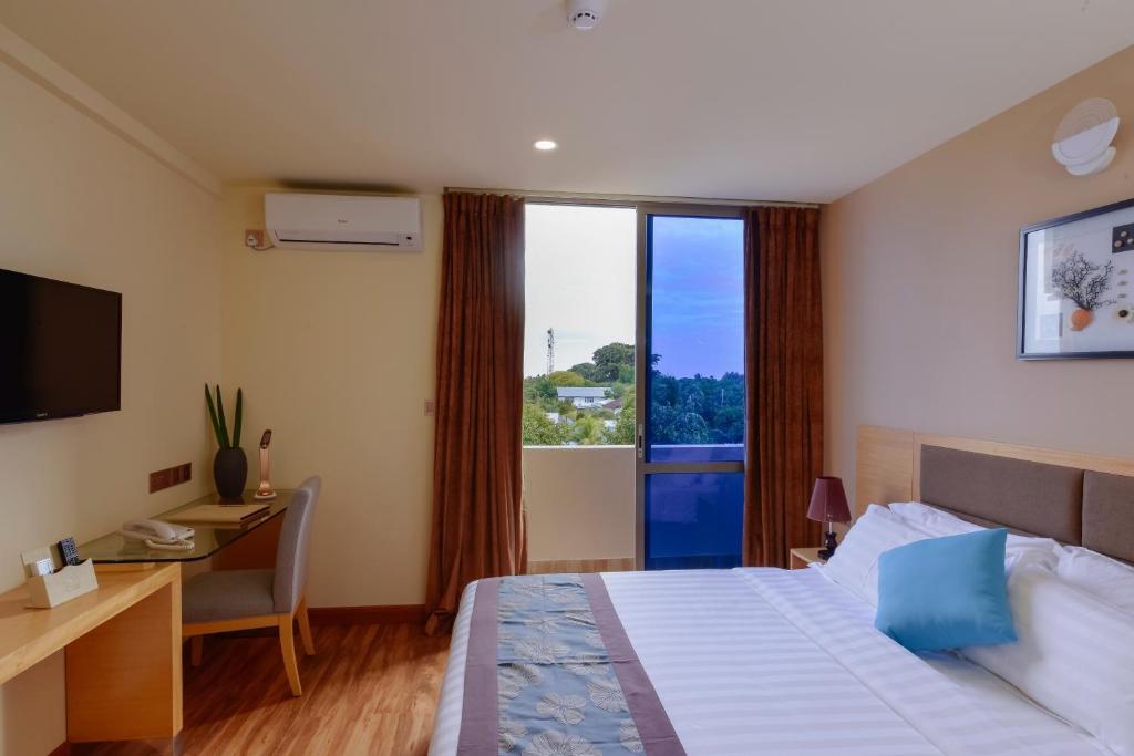 Mūsdienīgs viesnīcas numurs ar lielu logu, kurā ir gultas ar spilveniem un koka grīda. Uz galda atrodas klēpjdators un dekoratīvas augu kompozīcijas.