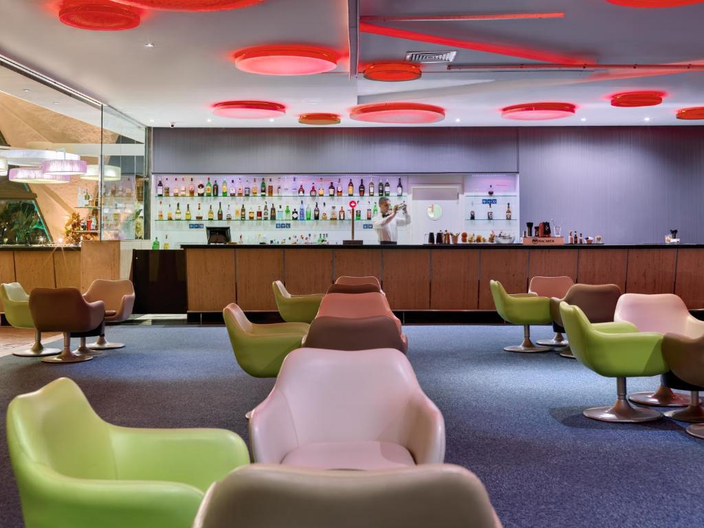 Mūsdienīgs bārs ar krāsainām krēslām un apgaismojumu, kas izceļ bāra letes un dzērienu plauktus. Komfortabla atmosfēra, ideāli piemērota relaksācijai un sociālām sanākšanām.