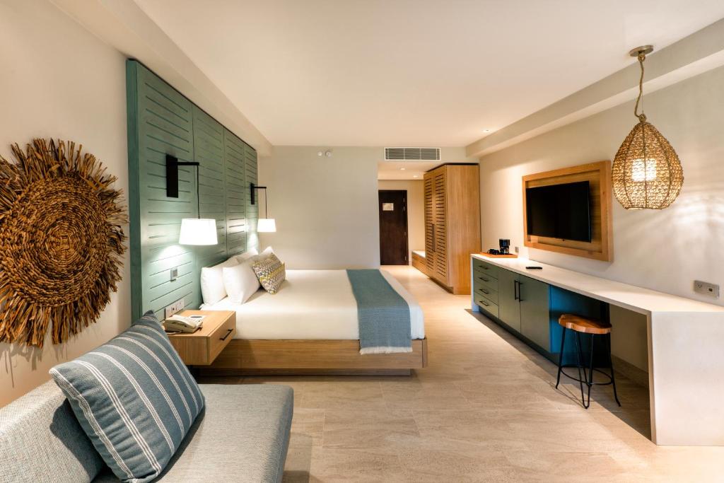 Mūsdienīga viesnīcas numura interjers ar gaisīgu dizainu, kurā ir liela gulta, dīvāns un televizors. Uzsvars uz dabīgiem materiāliem un siltām krāsām, radot relaksējošu atmosfēru.