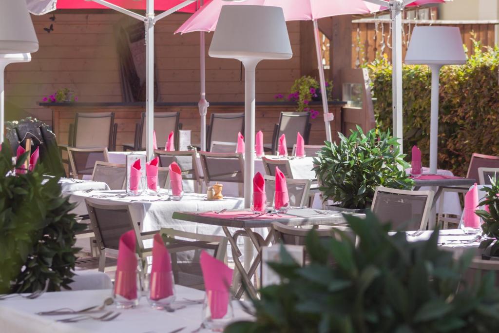 Āra restorāna terase ar baltiem galdiem un rozā salvetēm, apzaļumota ar augiem un saulessargiem. Ideāla vide relaksējošai maltītei.