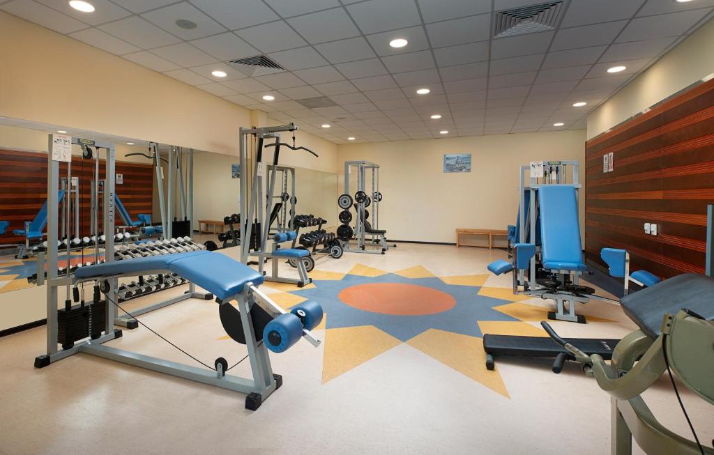 Mūsdienīga sporta zāle ar dažādām fitnesa iekārtām un trenažieriem, kas izvietoti uz krāsaina grīdas. Gaisma un plašums rada patīkamu treniņu vidi.