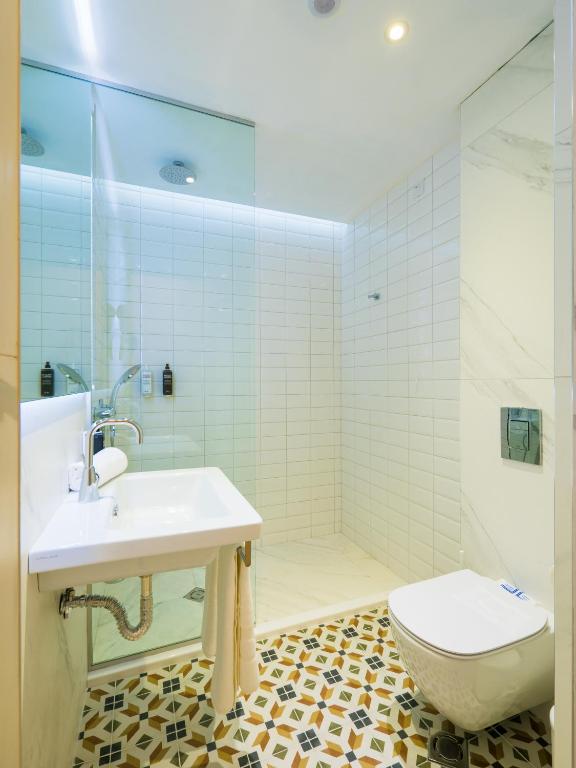 Mūsdienīga vannas istaba ar stikla dušu, baltiem flīzēm un rakstainu grīdu. Iekārtota ar minimālistisku izskatu un modernām santehnikas iekārtām.