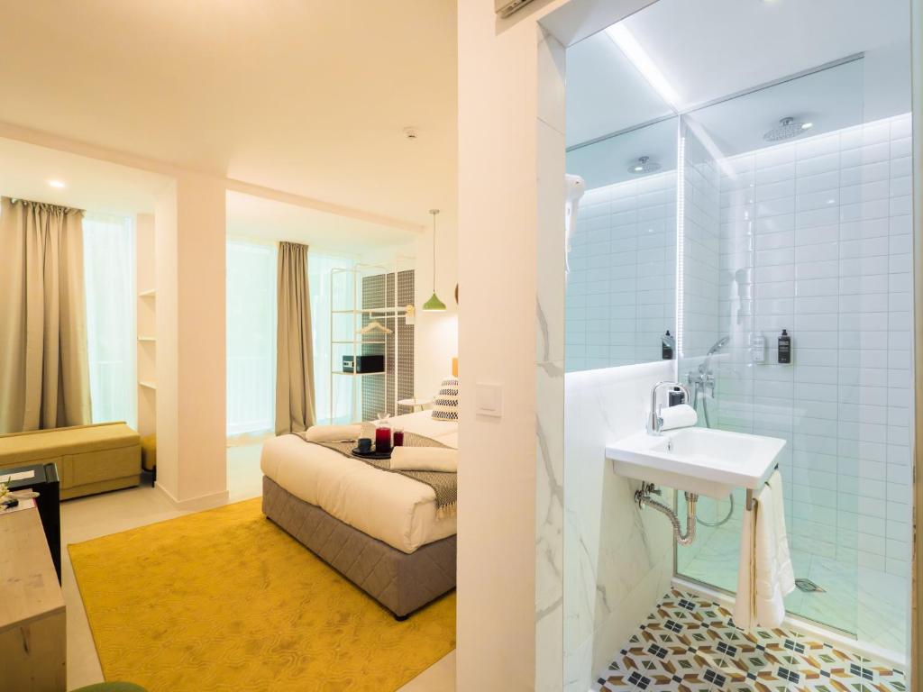 Mūsdienīga viesnīcas numura iekārtojums ar gultu, dīvānu un stikla dušu. Interjers ir gaišs un elegants, ar mūsdienīgu dizainu un jauku paklāju.