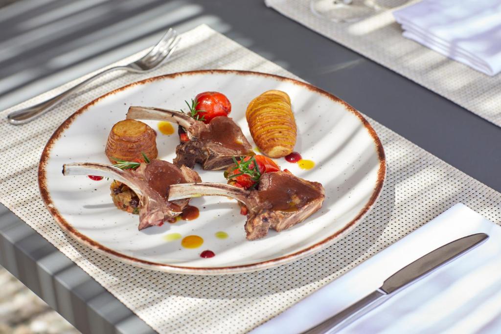 Gurķu šķēles ar jēra gaļu, ceptiem kartupeļiem un dārzeņiem, pasniegti uz elegantas šķīvja ar krāsainām mērcēm.