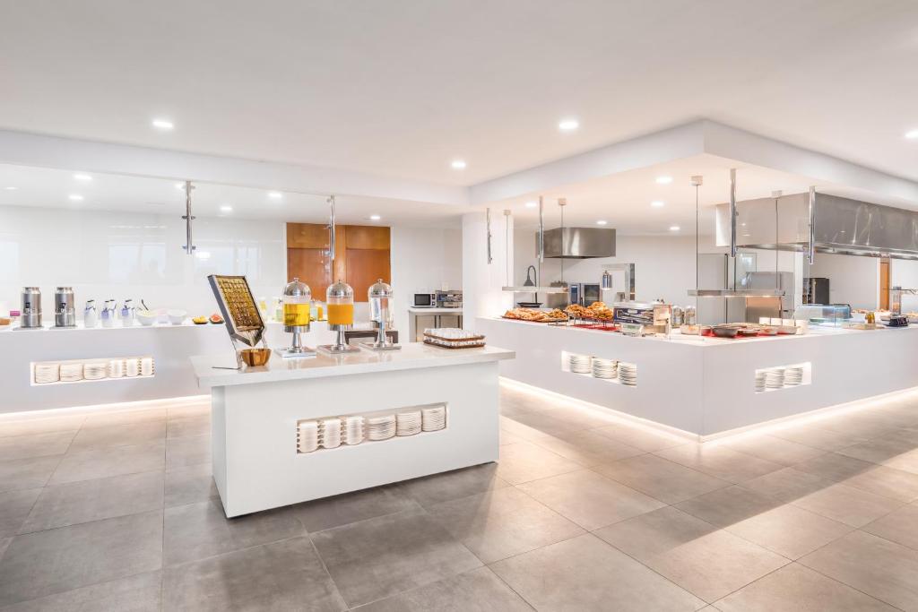 Mūsdienīga, gaiša virtuve ar plašu bufeti, kas piedāvā dažādus ēdienus un dzērienus. Apgaismojums un baltas virsmas rada tīru un elegantu atmosfēru.