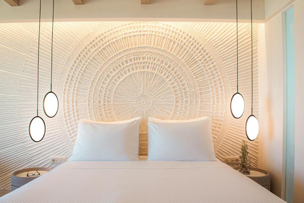 Mūsdienīgs guļamistabas interjers ar stilīgu gultu, apgaismojuma ķermeņiem un dekoratīvu sienu, kas rotāta ar teksturētu dizainu. Ideāla atmosfēra atpūtai un relaksācijai.