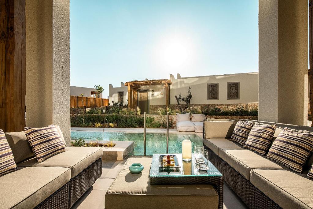 Eleganta terase ar komfortablu dīvānu un galdiņu, kas piedāvā skatu uz baseinu un saulainu dārzu. Ideāla vieta relaksācijai un atpūtai.