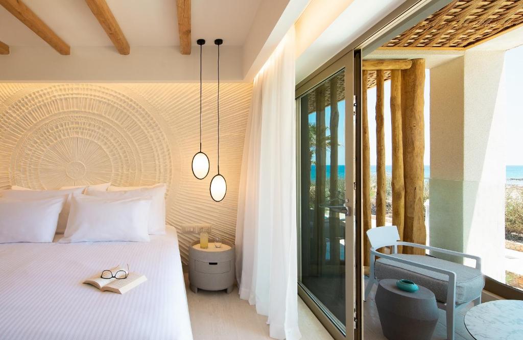 Mūsdienīgs viesnīcas numurs ar gaisīgu un elegantu interjeru, kurā ir gultas ar baltām gultasveļām, dekoratīvs sienas elements un skats uz jūru. Numurā ir arī ērta atpūtas zona ar krēslu un galdu.