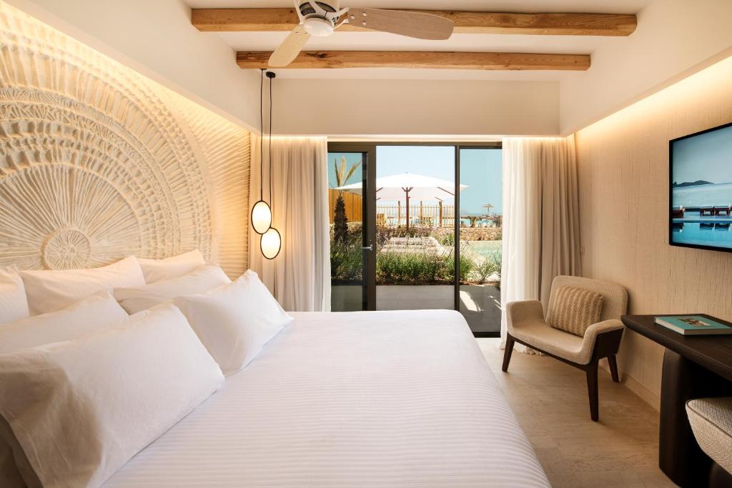 Moderns viesnīcas numurs ar elegantu interjeru, baltām gultasveļām un izsmalcinātu sienu apdari. No numura paveras skats uz dārzu un baseinu, radot relaksējošu atmosfēru.