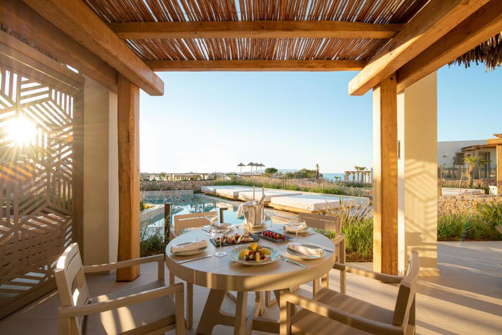 Mierīgā terase ar galdu, kas klāts ar gardām uzkodām, un skatu uz baseinu un jūru, apgaismots ar saules gaismu. Ideāla vieta relaksācijai un baudīšanai.