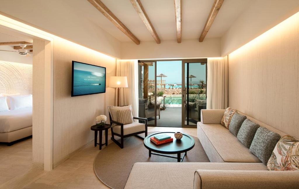 Mūsdienīga viesnīcas numura iekārtojums ar ērtu dīvānu, televizoru un skatu uz terasi ar baseinu. Gaismas un dabīgās krāsas radījušas relaksējošu atmosfēru.