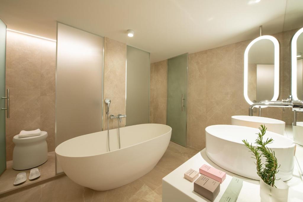 Mūsdienīgs vannas istabas interjers ar brīvo stāvošu vannu, mazgāšanas baseinu un elegantiem aksesuāriem. Gaismas apgaismojums un neitrālas krāsas rada relaksējošu atmosfēru.