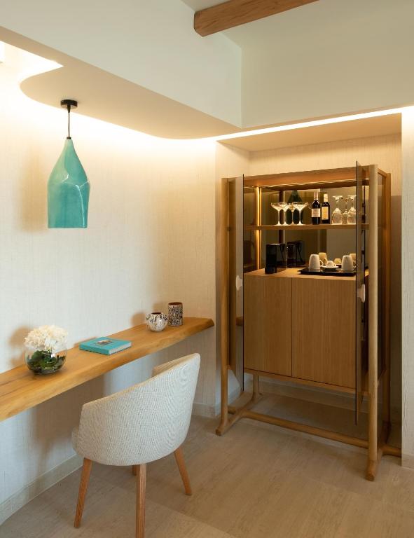 Mūsdienīgs interjers ar koka rakstāmgaldu, ērtu krēslu un elegantu bāra skapīti, kurā redzami glāzes un dzērienu pudeļu komplekti. Gaismas elementi piešķir telpai siltu atmosfēru.