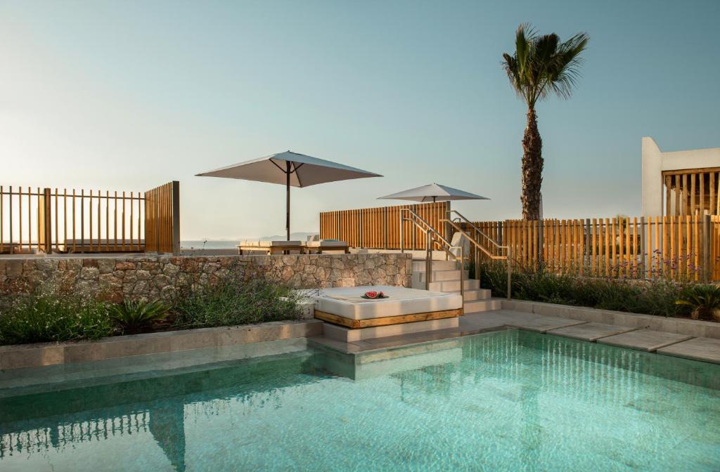 Luksuss baseins ar saules gultām un palmi, kas atrodas mierīgā vidē pie jūras, nodrošina ideālu vietu relaksācijai. Eleganta ainava ar koka žogu un ziediem papildina mierīgo atmosfēru.