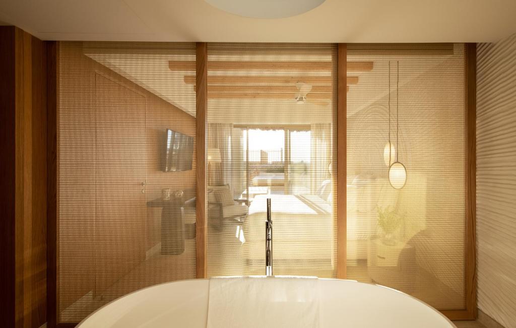 Mūsdienīga vannas istaba ar stiklotu starpsienu, kas nodala vannu no viesistabas, kurā ir dabiska gaisma un eleganta interjera elementi.