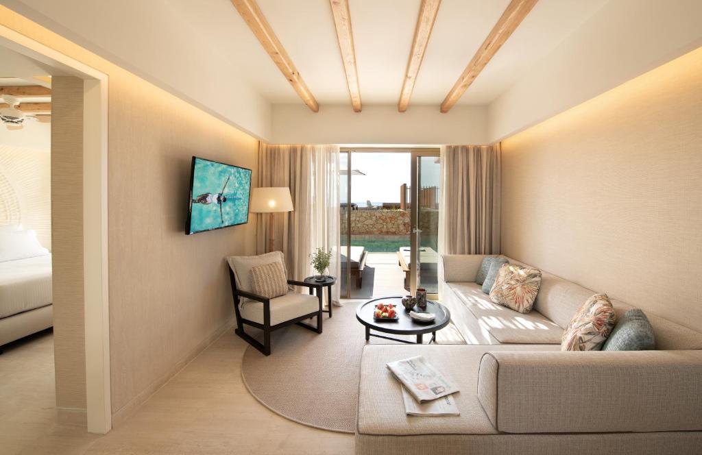 Mūsdienīgs viesnīcas numurs ar gaišu interjeru, ērtu dīvānu un televizoru, kas piedāvā skatu uz terasi ar atpūtas zonu. Numurs ir apgaismots ar dabīgu gaismu un ir eleganti noformēts.