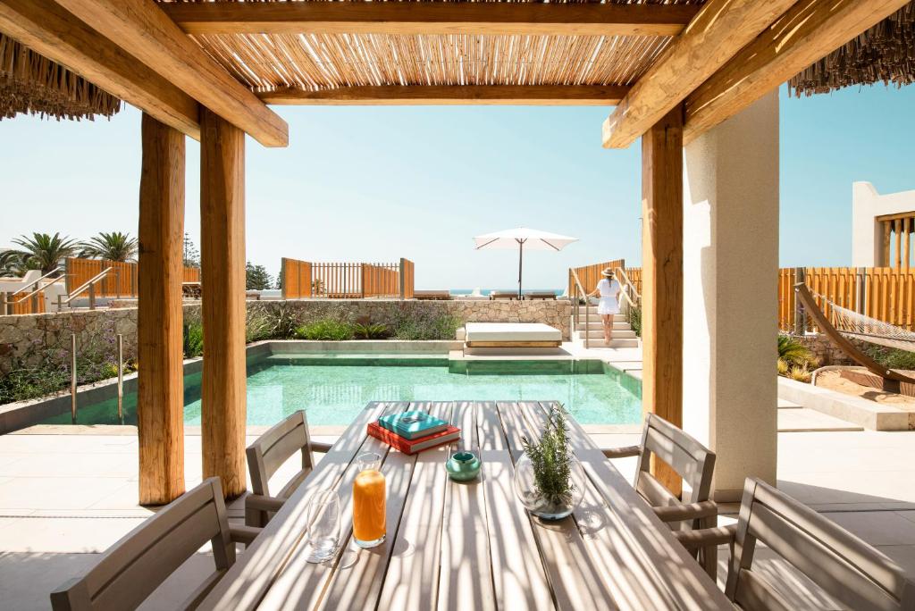 Mūsdienīgs āra atpūtas laukums ar baseinu, koka terasi un ērtu galdu, kurā atrodas dzērieni un grāmatas. Fons ar saulainu laiku un pludmales skatu.