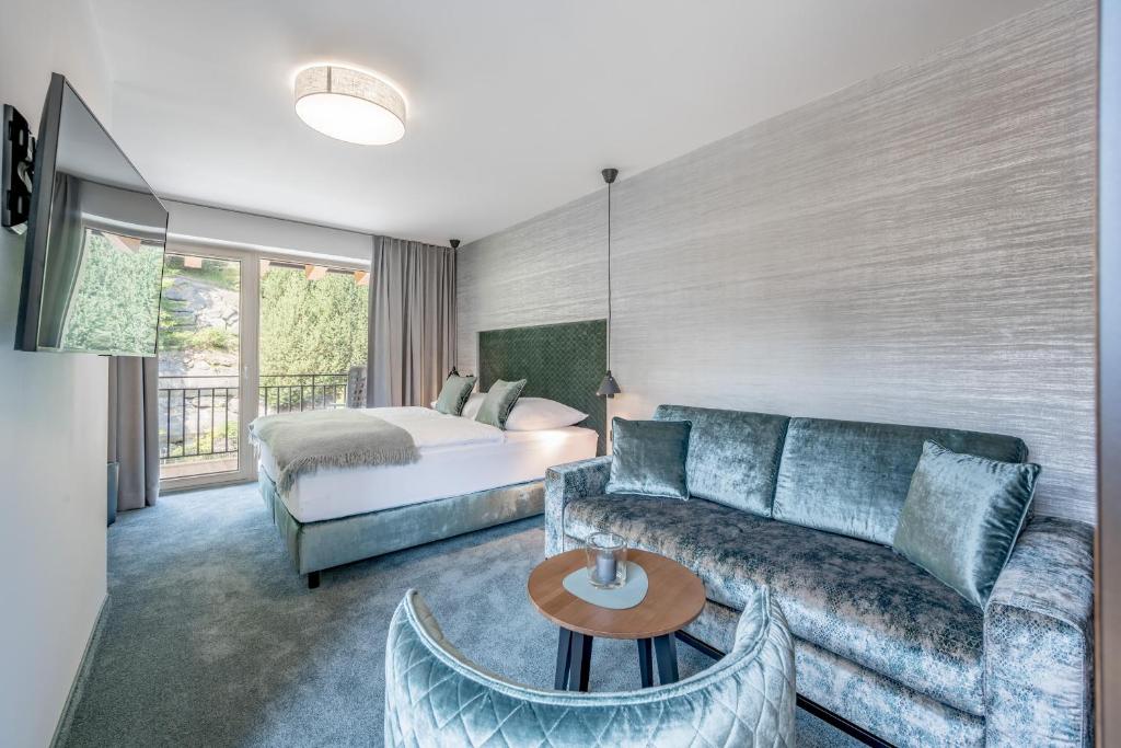 Mūsdienīgs viesnīcas numurs ar ērtu gultu, dīvānu un balkonu, caur kuru ienāk dabiska gaisma, radot patīkamu atmosfēru.