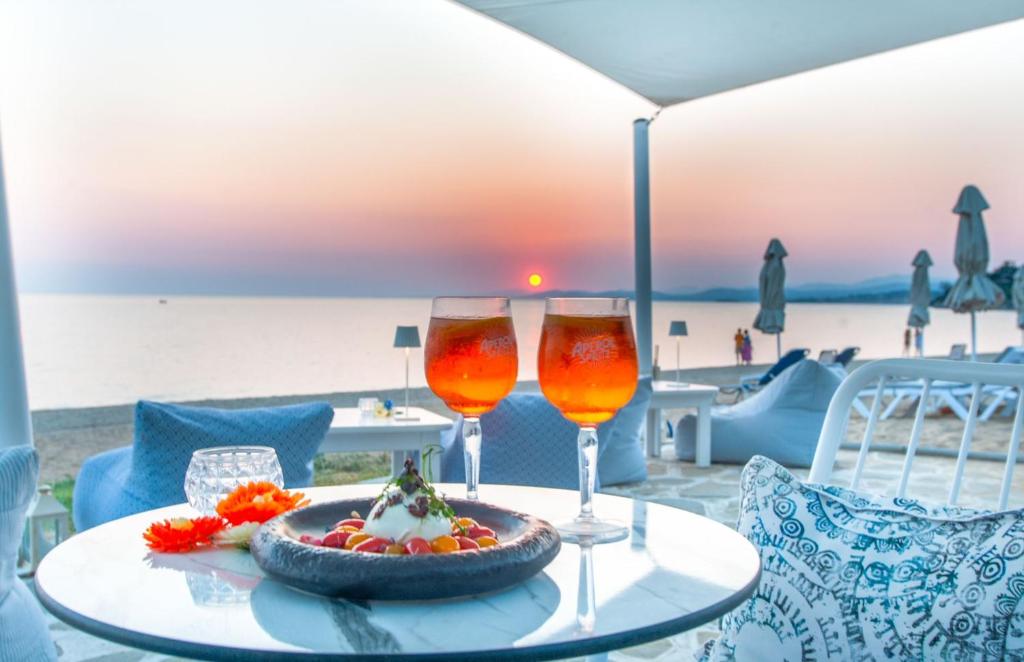 Saulrieta skats pie pludmales ar divām glāzēm dzēriena un desertu uz galda, kas izveidots relaksējošā atmosfērā.
