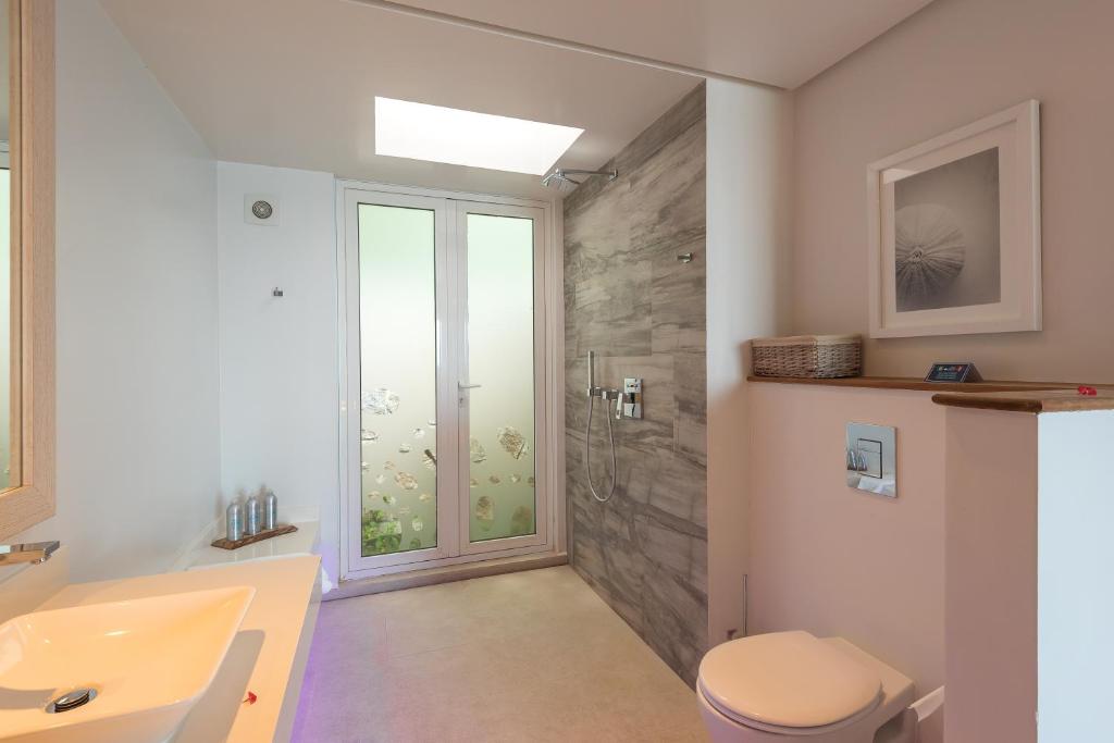 Mūsdienīgs vannas istabas interjers ar stikla durvīm un dušu, gaišām krāsām un minimālistisku dizainu. Redzami higiēnas piederumi un dekori, kas piešķir telpai svaigumu.