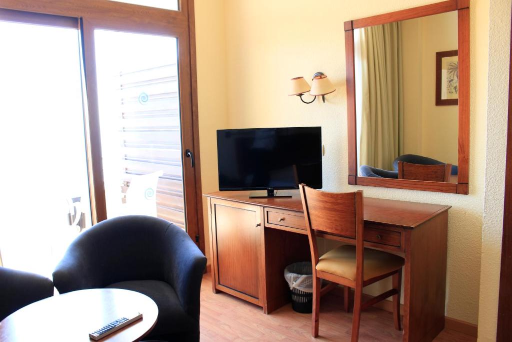 Mūsdienīgs viesnīcas numurs ar koka mēbelēm, televizoru un spoguli, kas atrodas blakus logam. Telpa ir gaiša un ērta, ar rakstāmgaldu un krēslu.