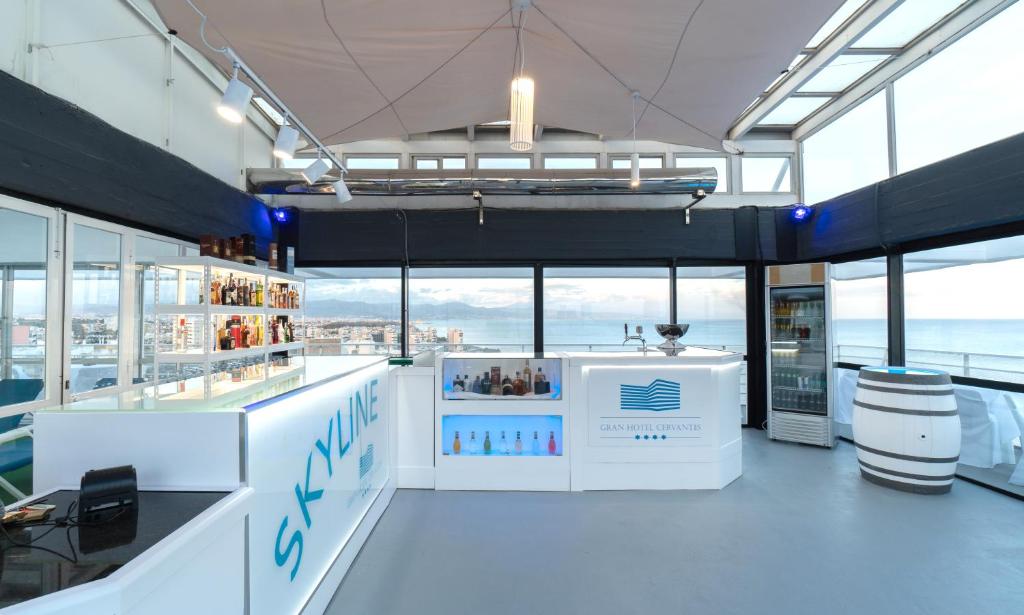 Mūsdienīgs bārs ar panorāmas logiem, kas atrodas augstajā stāvā. Skats uz jūru un pilsētu, moderns interjers ar gaišām krāsām un elegantu apgaismojumu.