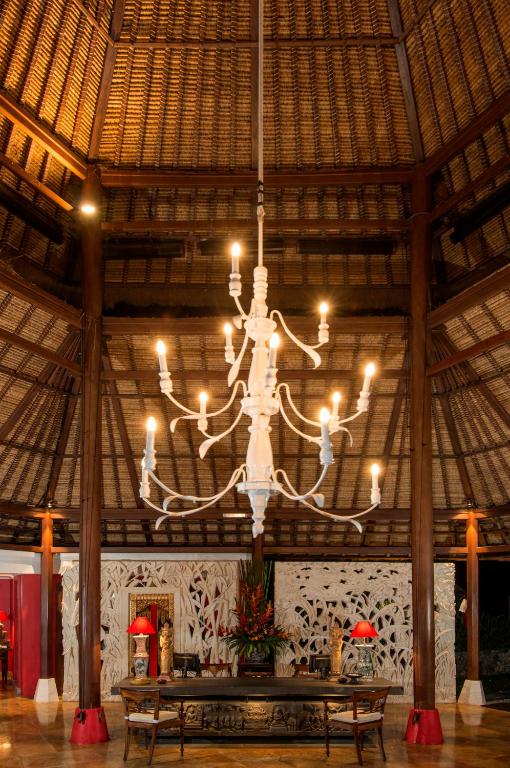 Elegants lustra ar astoņām spuldzēm, kas karājas stikla un koka interjerā, radot siltu un viesmīlīgu atmosfēru. Fons satur dekoratīvas augu kompozīcijas un stilīgas mēbeles.