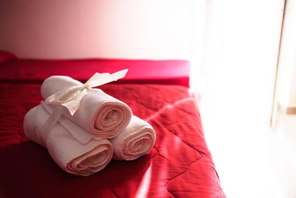 Skaisti salocīti dvieļi ar lentīti, novietoti uz sarkanā gultas pārklāja. Gaismas plūsmā radīta mājīga un relaksējoša atmosfēra.