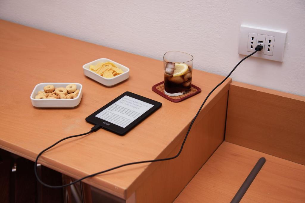 Koka galds ar e-grāmatu, uzkodu traukiem un dzērienu, kas pievienots elektrības kontaktligzdai.