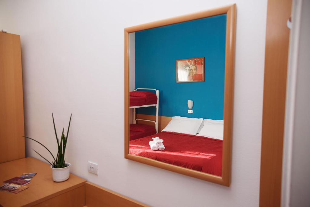 Apskatāma moderna guļamistaba ar sarkanu gultu un divstāvu gultu, kuru atspoguļo spogulis. Sienas ir krāsotas spilgti zilā krāsā, un telpā ir arī istabas augs.