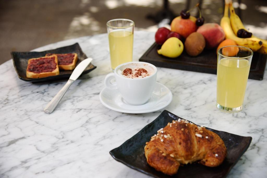 Brota galds ar krēmīgu kafiju, sviestmaizēm, kruasānu un augļiem, kas pasniegti uz marmora galda.