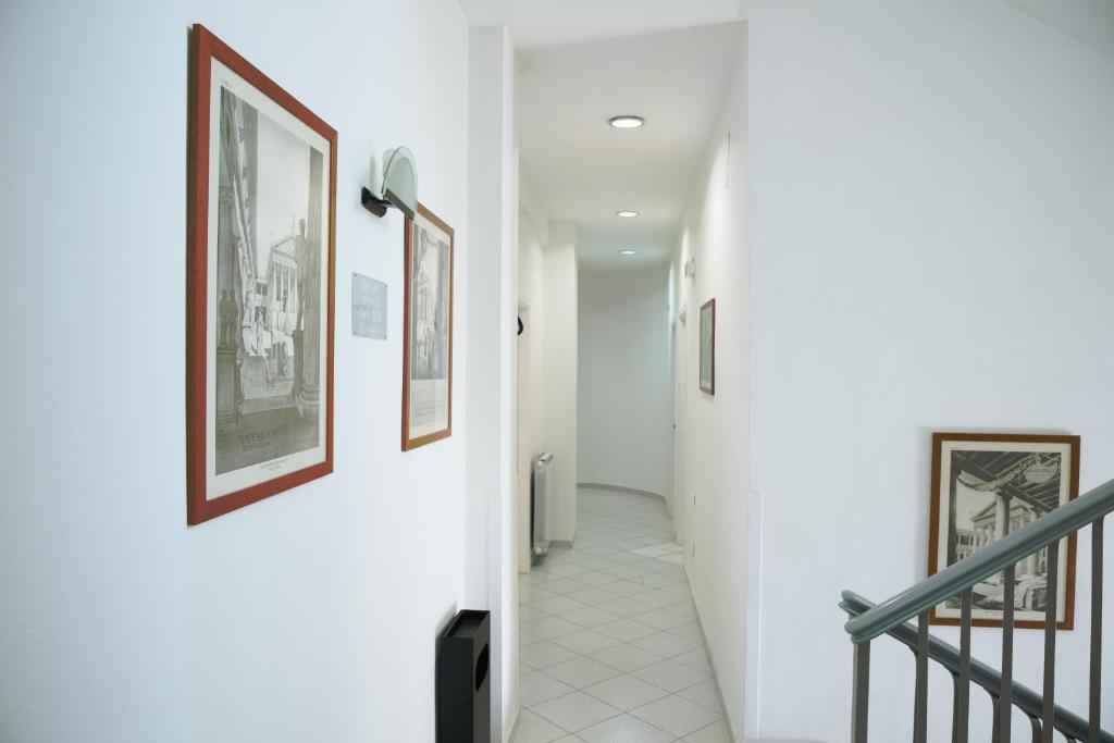 Gaišs gaiteņs ar pie sienām piekārtām grafiskām ilustrācijām un slīpu kāpņu margu.