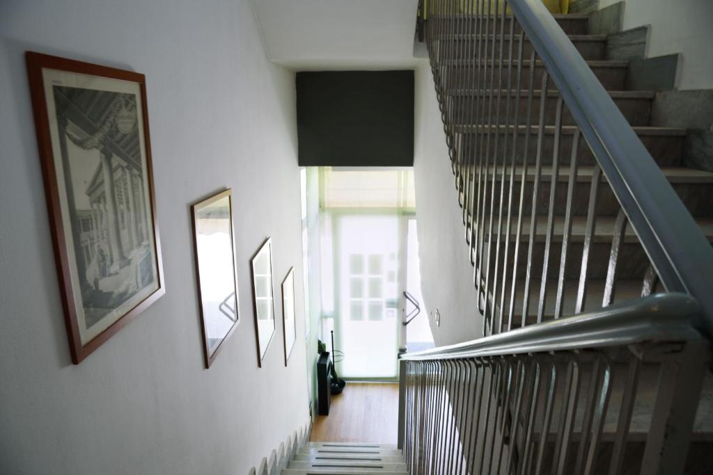 Kāpņu telpa ar gleznām uz sienām un logu, kas ved uz ārpusi. Kāpnes ir ar metāla margām un koka grīdu.