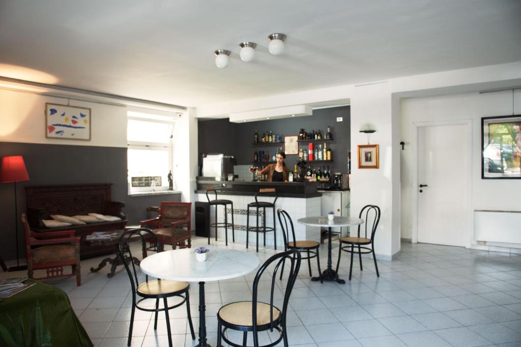 Moderns kafejnīcas interjers ar bāru, ērtu sēdvietu zonu un gaisīgu atmosfēru. Aiz bāra stāv apkalpojošais personāls, bet uz galdiem ir izkārtoti krēsli un galdi.