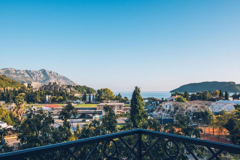 Skats uz jūru un kalniem no balkona, ar zaļām kokiem un pilsētas ainavu. Skaidrs debesis un mierīga atmosfēra.