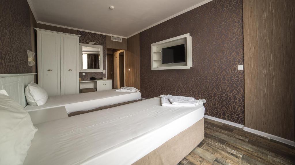 Mūsdienīgs viesnīcas numurs ar divām gultām, elegantām tapetēm un televizoru uz sienas. Gaisīgs interjers ar skapi un rakstāmgaldu.