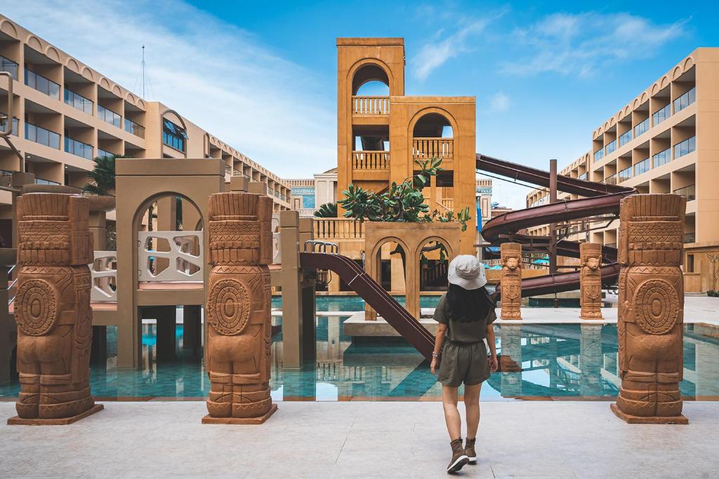 Vasaras atpūtas komplekss ar baseinu un ūdens slidkalniņiem, ko ieskauj tropiski augi un dekoratīvi akmens skulptūras.