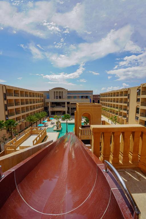 Vizuālā skata uz viesnīcas baseinu un ūdens slidkalniņu, kas izveidots ar siltām krāsām un apkārtējiem kokiem. Skaists laika apstākļu fons ar zilu debesu un mākoņu kombināciju.