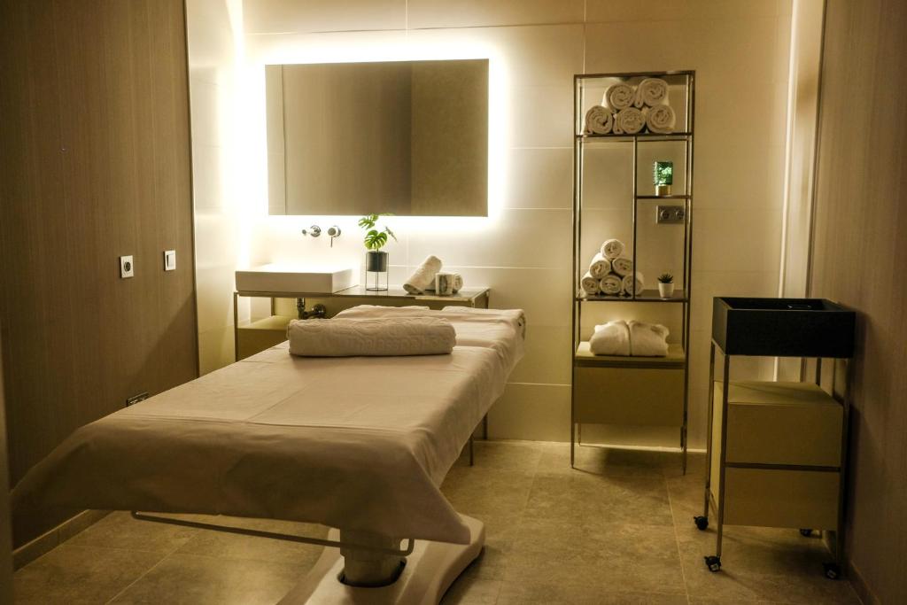 Mūsdienīgs masāžas kabinets ar relaksējošu atmosfēru, baltiem dvieļiem un elegantu interjeru. Telpā ir gaismas apgaismojums un augi, kas veicina mierīgu noskaņu.