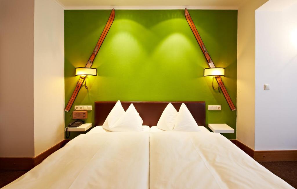 Guļamistabas interjers ar zaļām sienām, divām gultām un slēpošanas inventāra dekorācijām. Gaismas elementi rada mājīgu atmosfēru.