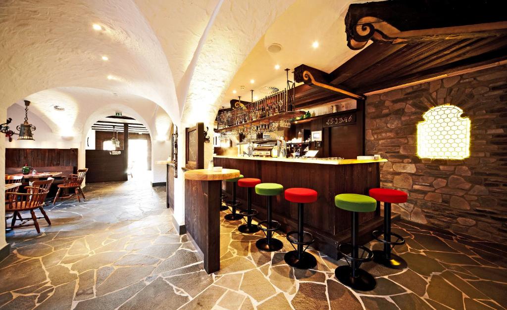 Mūsdienīgs bārs ar koka interjeru un krāsainām krēslām, kas rada siltu un aicinošu atmosfēru. Gaismas un akmens grīdas dizains piešķir unikālu raksturu šai telpai.