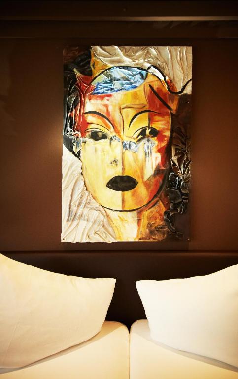 Kunsts darbs ar sejas attēlu, izceļot spilgtas krāsas un unikālu stilu, novietots uz tumšas sienas, blakus divām baltām spilveniem.