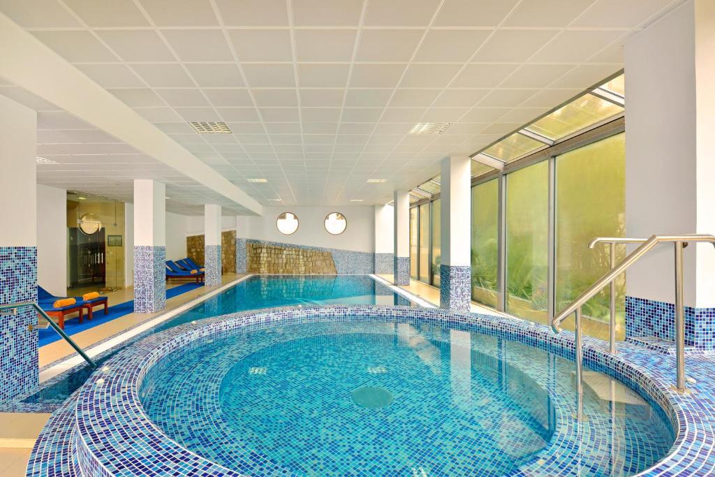 Mūsdienīgs iekštelpu peldbaseins ar zilajiem mozaīkas flīzēm, apgaismojums un relaksācijas zona. Liels logs nodrošina dabisko apgaismojumu un skatījumu uz apkārtni.